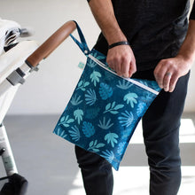 Load image into Gallery viewer, A person zips a Bumkins Wet Bag: Blue Tropic attached to a stroller handle in a bright room.