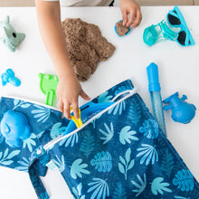 Load image into Gallery viewer, A child plays with kinetic sand and blue beach toys near a Bumkins Wet Bag: Blue Tropic on a white table.