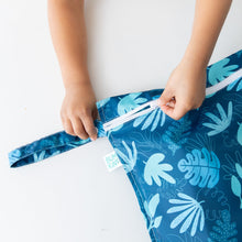 Load image into Gallery viewer, Close-up of a child zipping a Bumkins Wet Bag: Blue Tropic on a white table.