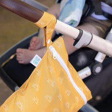 Load image into Gallery viewer, Bumkins Wet Bag: Sunshine is attached to a stroller with baby's legs visible, featuring sun patterns and a smooth zipper closure.