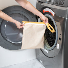 Load image into Gallery viewer, A person holds a Bumkins Wet Bag: Sunshine in front of a gray front-load washing machine.