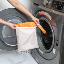 Load image into Gallery viewer, A person holds a Bumkins Wet Bag: Grounded in front of an open front-loading washing machine.