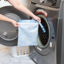 Load image into Gallery viewer, A person holds Roamio by Bumkins Wet Bag: Vintage Denim in front of an open front-loading washing machine.