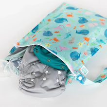 Load image into Gallery viewer, Bumkins Wet Bag: Ocean Life lays on a white background, with cloth diapers and breast pump parts peeking out.