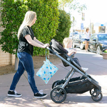 Load image into Gallery viewer, A woman pushes a child in a stroller on a sunny sidewalk, with a Bumkins Wet Bag: Ocean Life attached to the handle.