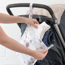 Load image into Gallery viewer, Hands place clothes into a Bumkins Wet Bag: Floral hanging on a stroller handle in front of a white brick wall.