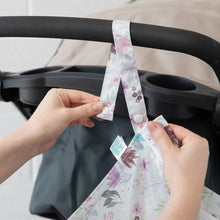 Load image into Gallery viewer, Close-up of hands attaching a Bumkins Wet Bag: Floral to a stroller with the snap button on the handle.