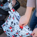 A person zips a Bumkins Wet Bag: Mickey Mouse Classic attached to a stroller handle.