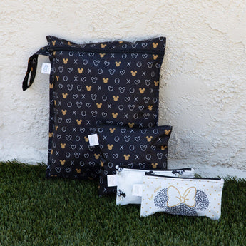Bumkins Wet Bag: Minnie Mouse Icon Black + White sits on grass against a beige textured wall with three smaller bags.
