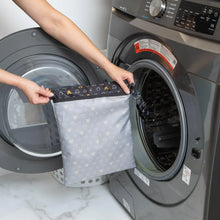 Load image into Gallery viewer, A person holds Bumkins Wet Bag: Minnie Mouse Icon Black + White in front of an open front-loading washing machine.