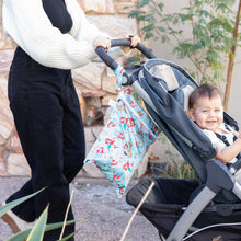 Load image into Gallery viewer, A person pushes a smiling baby in a stroller with a Bumkins Wet Bag: Disney Princess Ariel hanging from the handle.