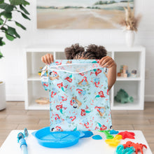 Load image into Gallery viewer, A child lifts a colorful Bumkins Wet Bag: Disney Princess Ariel at a white table with vibrant blue and red toys.
