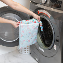 Load image into Gallery viewer, A person holds a Bumkins Wet Bag: Disney Princess Ariel in front of an open front-loading washer next to a white laundry basket.