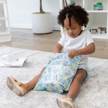 Load image into Gallery viewer, A young child with curly hair opens a bag from Bumkins Wet Bag: Aloha Stitch while sitting on a gray rug.