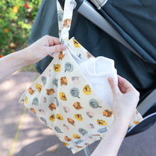 Load image into Gallery viewer, Close-up of hands placing a cloth into a Bumkins Wet Bag: Winnie and Friends hanging from a stroller handle outdoors