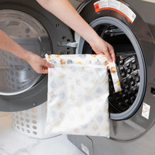 Load image into Gallery viewer, A person holds Bumkins Wet Bag: Winnie and Friends in front of a front-loading washing machine.