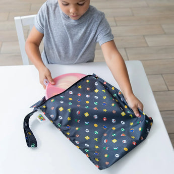 A child places a pink plate into a Bumkins Wet Bag: Super Mario™ Lineup at a white table.
