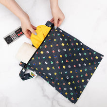 Load image into Gallery viewer, Hands place items into a Bumkins Wet Bag: Super Mario™ Lineup, with an NES controller teether beside it on a marble background.