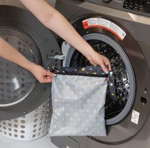 Load image into Gallery viewer, A person holds Bumkins Wet Bag: Super Mario™ Lineup in front of an open front-loading washing machine.