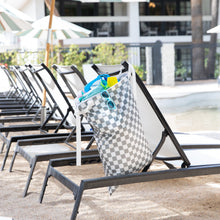 Load image into Gallery viewer, Bumkins Extra Large Wet Bag: Charcoal Check hangs on a poolside lounge chair with sunglasses and swimwear; nearby are chairs and umbrellas.