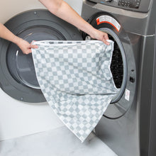 Load image into Gallery viewer, A person loading a Bumkins Extra Large Wet Bag: Charcoal Check into an open washing machine.