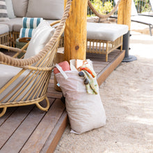 Load image into Gallery viewer, Bumkins Extra Large Wet Bag: Wander, filled with beach essentials, sits by wicker seating on a wooden deck framed by sand and rope.