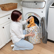 Load image into Gallery viewer, A person kneels by a front-load washer, placing colorful clothes into a Bumkins Extra Large Wet Bag: Winnie + Friends.