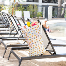 Load image into Gallery viewer, Bumkins Extra Large Wet Bag: Winnie + Friends filled with beach essentials hangs from an empty lounge chair near a pool.