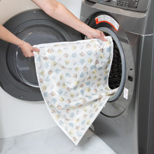 Load image into Gallery viewer, A person places a Bumkins Extra Large Wet Bag: Winnie + Friends into an open front-loading washing machine.