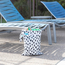 Load image into Gallery viewer, Bumkins Wet/Dry Bag: Hearts sits by blue lounge chairs, holding towels and pool essentials.