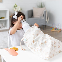 Load image into Gallery viewer, A child in a white shirt places a water bottle into a Bumkins Wet/Dry Bag: Palm Daze, with sand toys on the white table nearby.