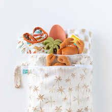 Load image into Gallery viewer, Bumkins Wet/Dry Bag: Palm Daze holds clothes, silicone toys, crab plush, and patterned cloth on a white background.