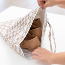 Load image into Gallery viewer, A child's hands open a Bumkins Wet/Dry Bag: Sand Check on a white table, revealing brown shoes inside.