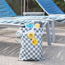 Load image into Gallery viewer, Bumkins Wet/Dry Bag: Charcoal Check holds sunglasses, a water bottle, and swim essentials next to two empty lounge chairs.