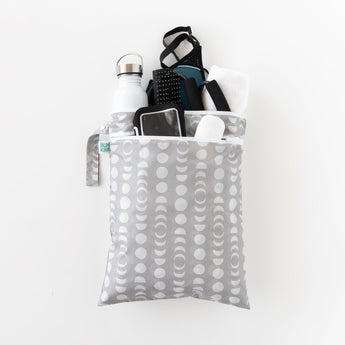 Bumkins Wet/Dry Bag: Lunar Phase holds gym essentials like a bottle, phone, towel, clothes and toiletries on a white background.