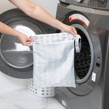 Load image into Gallery viewer, A person holds a Bumkins Wet/Dry Bag: Lunar Phase in front of an open front-loading washing machine.