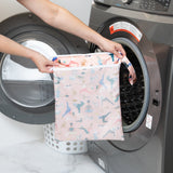 A person holds a Bumkins Wet/Dry Bag: Yoga Pals in front of a front-loading washing machine.