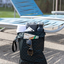 Load image into Gallery viewer, Roamio by Bumkins Wet/Dry Bag: Rich Black holds sunglasses, a book, towel, and water bottle by empty blue lounge chairs.