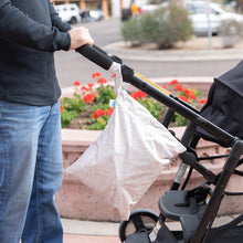 Load image into Gallery viewer, Someone pushes a stroller with Bumkins Wet/Dry Bag: Wander attached, surrounded by urban scenery and a flowerbed.