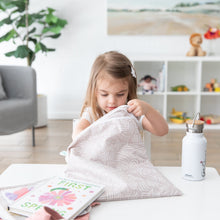 Load image into Gallery viewer, A young girl reaches into a Bumkins Wet/Dry Bag: Wander at a white table with books and water bottle in a bright, plant-filled room.