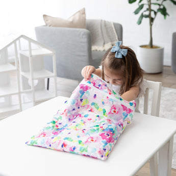 A young girl opens a Bumkins Wet/Dry Bag: Watercolor at a white table in a bright, modern living room.