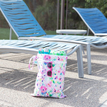 Load image into Gallery viewer, Bumkins Wet/Dry Bag: Watercolor holds pool items and pink sunglasses by blue lounge chairs on a sunny patio.