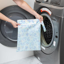 Load image into Gallery viewer, A person holds a Bumkins Wet/Dry Bag: Aloha Stitch in front of a front-loading washing machine.
