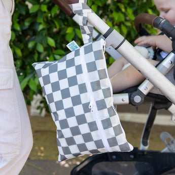 Bumkins Wet/Dry Clutch: Charcoal Check hangs from a stroller handle as a baby sits inside, pushed by an adult dressed in white.