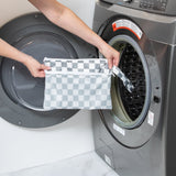 A person holds a Bumkins Wet/Dry Clutch: Charcoal Check by an open washing machine.