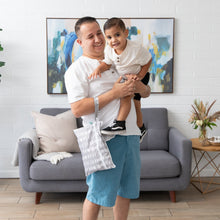 Load image into Gallery viewer, A man smiles holding a young boy by a gray sofa, with a Bumkins Wet/Dry Clutch: Lunar Phase on his arm.