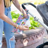 Under sunny skies, someone in jeans tucks wipes into a colorful Bumkins Wet/Dry Clutch: Boots attached to a stroller amidst greenery.