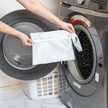 Load image into Gallery viewer, A person holds Roamio by Bumkins Wet/Dry Clutch: Disco Check in front of an open front-loading washing machine.
