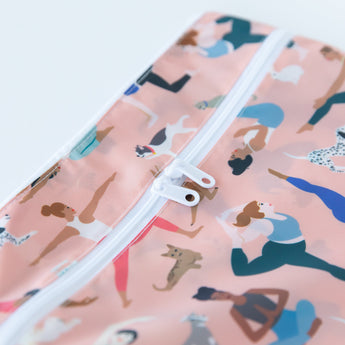 Close-up of Bumkins Wet/Dry Clutch: Yoga Pals, with a white zipper and yoga-themed pattern, made from waterproof fabric.