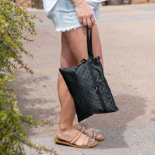 Load image into Gallery viewer, A woman in shorts and sandals holds a Roamio by Bumkins Wet/Dry Clutch: Rich Black outdoors by greenery.